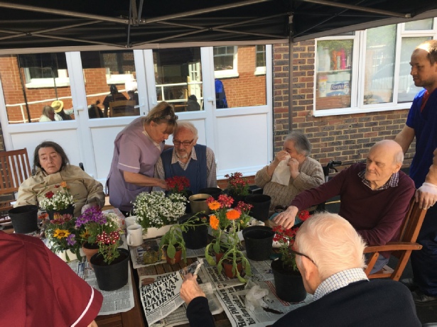 Group of Residents sitting around large table being helped to read newspapers and helped with potting plants